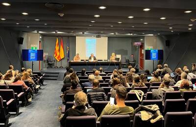 pla general de l'auditori de l'AMB amb els assistents asseguts i al fons la taula amb tres ponents